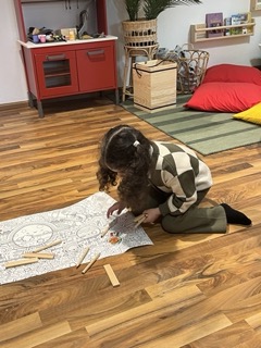 Ein Mädchen in der Sprachschule mit Plapagei sitzt auf dem Boden und malt ein Ausmalbild.